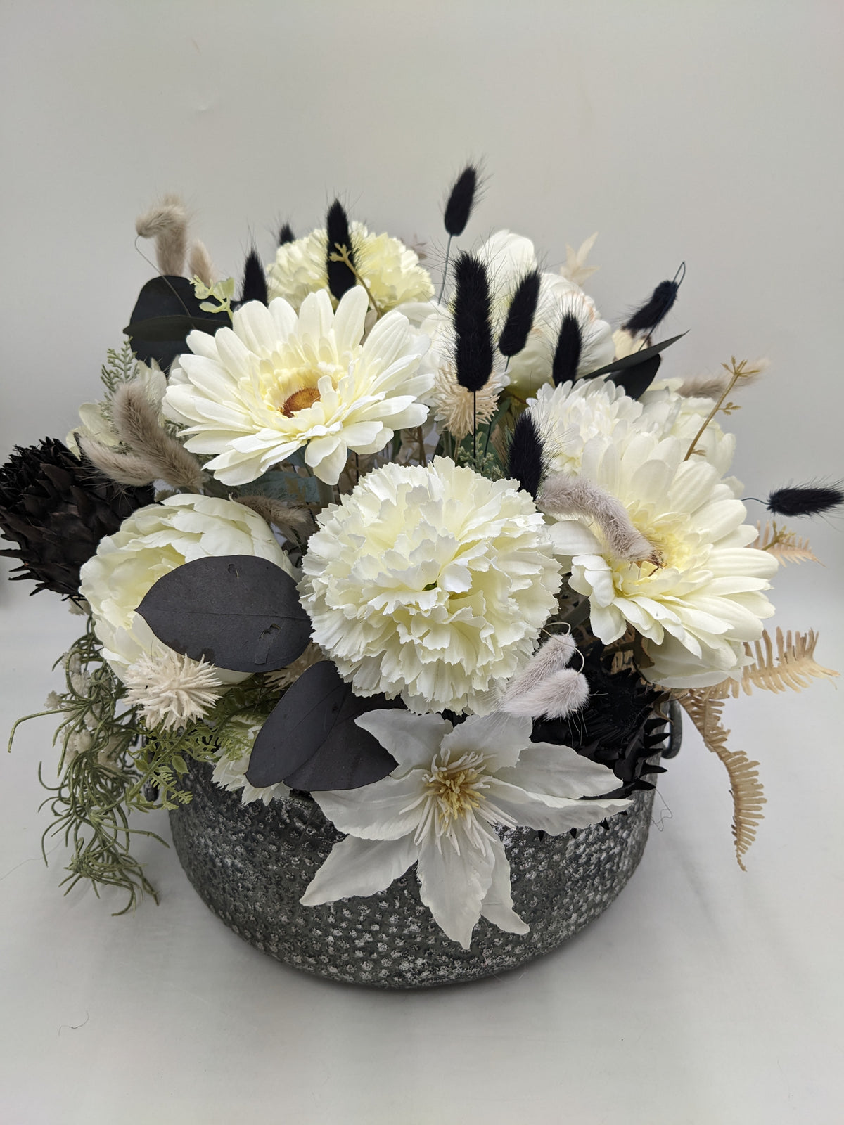 Gesteck in Weiß und Schwarz von vorne: Gerbera, Nelken, dunkle Eukalyptusblätter und heller Farn in runder Schale