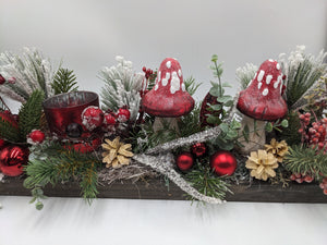 Weihnachtsgesteck aus der Nähe: rote Fliegenpilze, rotes Teelichtglas, rote Kugeln, Beeren, Zapfen und Tannenzweige