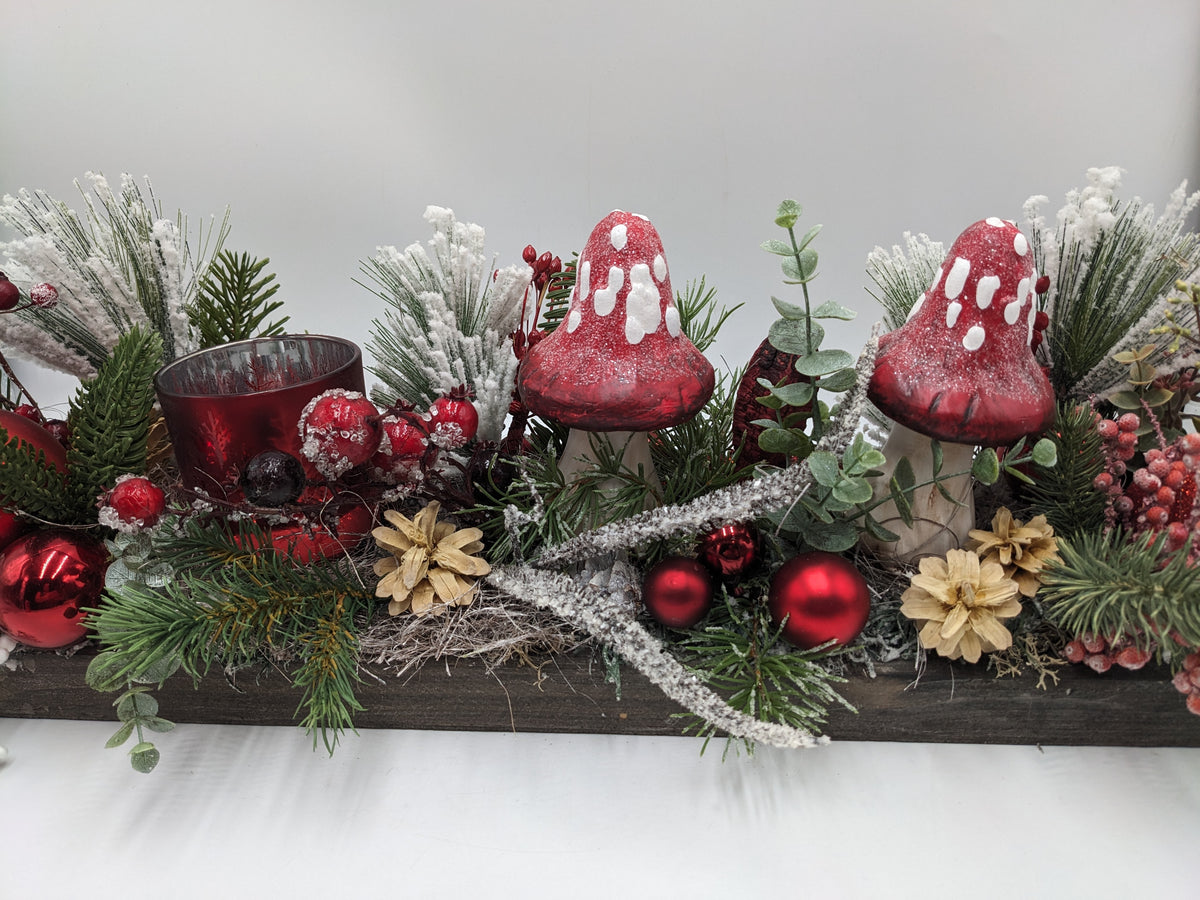 Weihnachtsgesteck aus der Nähe: rote Fliegenpilze, rotes Teelichtglas, rote Kugeln, Beeren, Zapfen und Tannenzweige