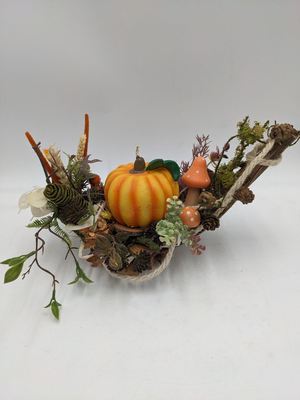 Flaches Herbstgesteck im Zweigschiffchen mit gelb-oranger Kürbiskerze, orangen Pilzen, Zapfen und Moos