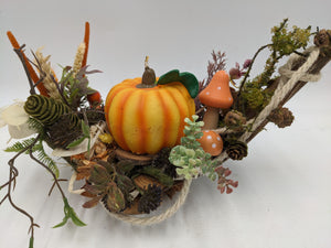 Herbstgesteck von vorn: Kürbiskerze auf Holzscheibe, zwei Fliegenpilze, Farn, Ähren und Kordel am Zweigrand