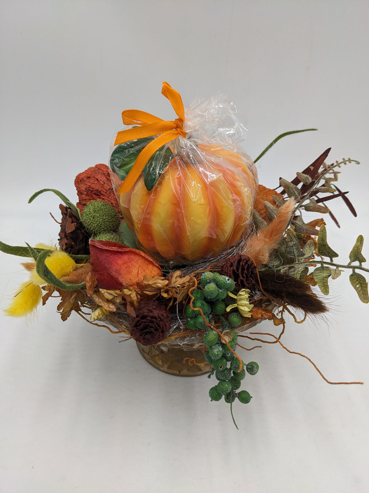 Herbstgesteck von oben: Kürbiskerze mit oranger Schleife, rote Blüte, gelbe Gräser und grüne Beerenranke
