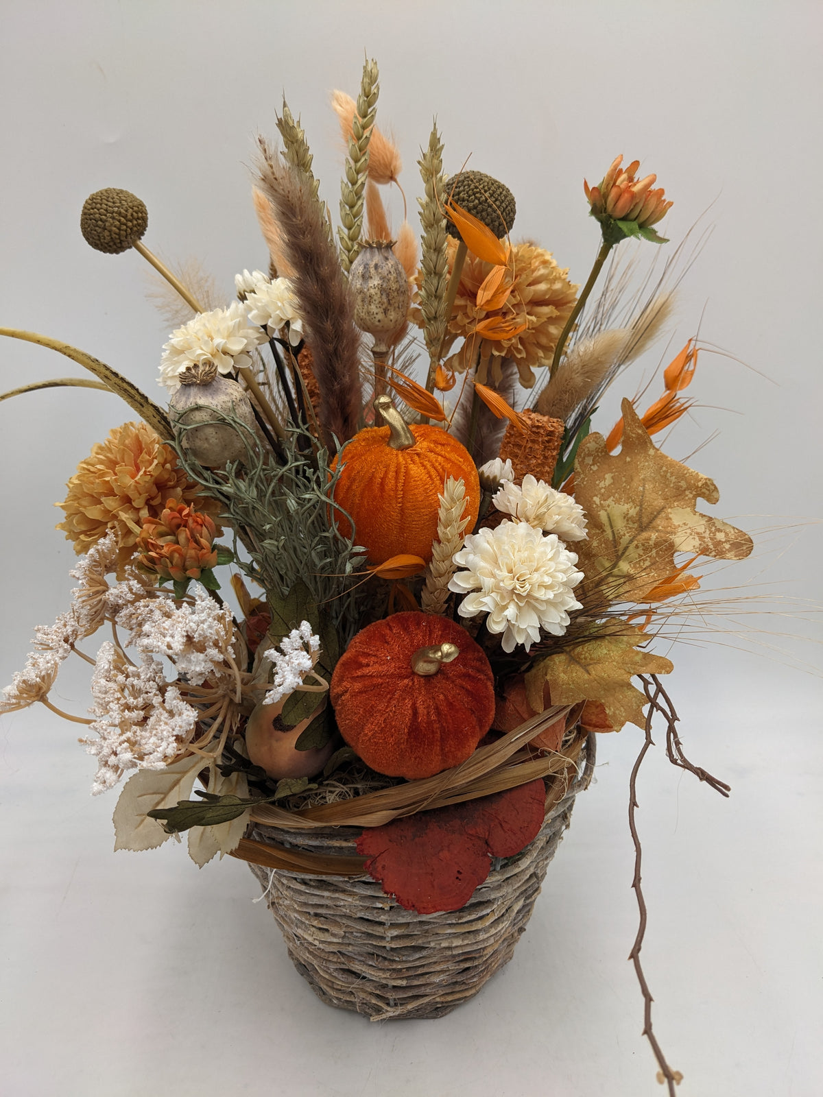 Herbstliches Korbgesteck von vorne: zwei Samtkürbisse, Craspedia, Eichenlaub und Pampasgras in Orange und Creme