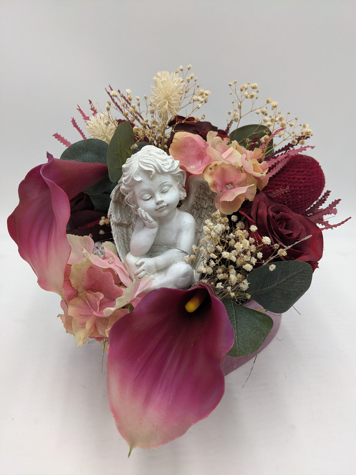 Trauergesteck mit weißer Engelfigur, beerenfarbenen Callas, dunkelroten Rosen und Schleierkraut