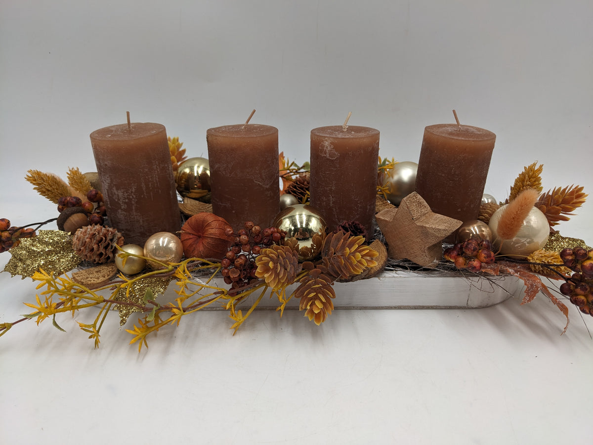 Längliches Adventsgesteck mit vier braunen Kerzen, goldenen Kugeln, Zapfen und Kürbis im weißen Holztablett