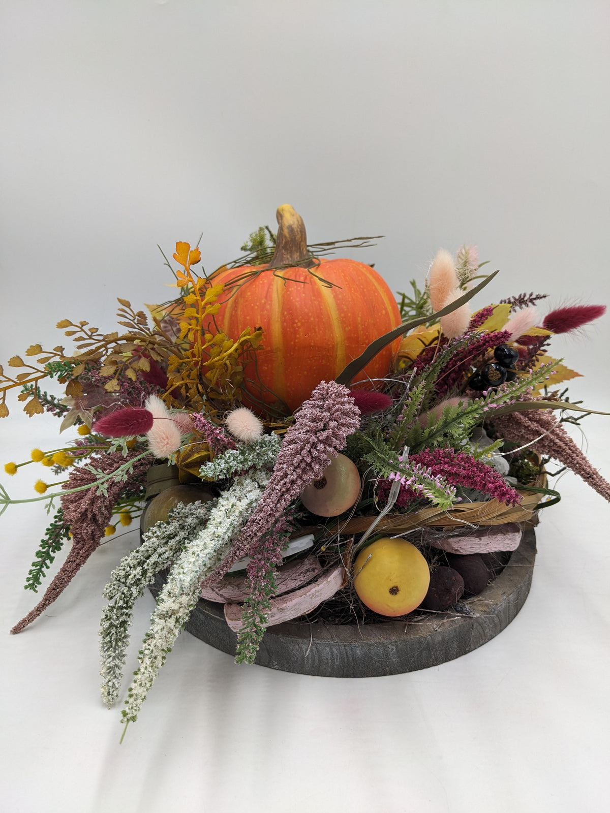 Herbstgesteck mit orangefarbenem Kürbis, Heide, rosa Gräsern und hängenden Amarantranken auf Holztablett