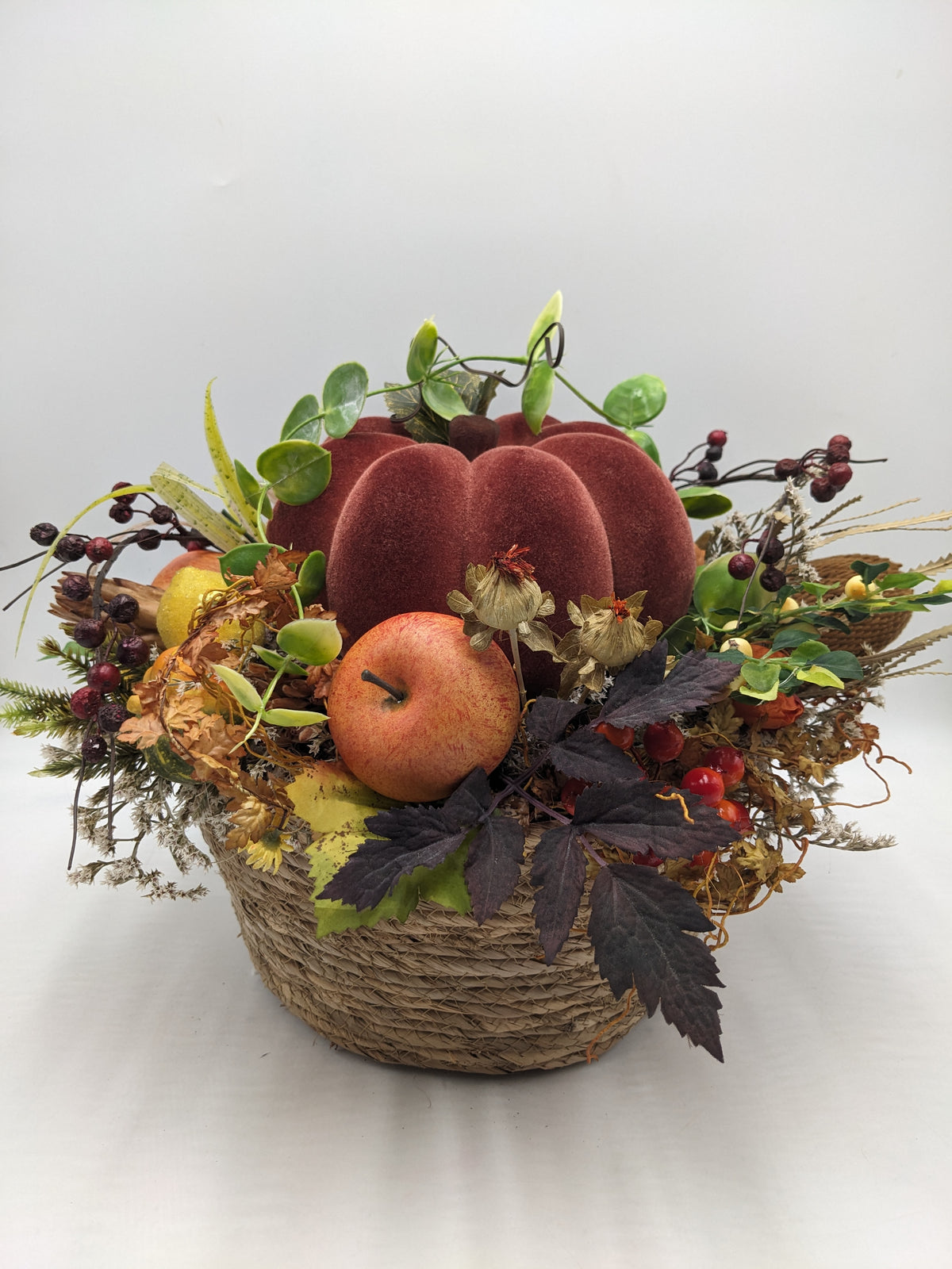 Herbstgesteck im Naturkorb mit rotbraunem Samtkürbis, Apfel, Beeren und buntem Herbstlaub