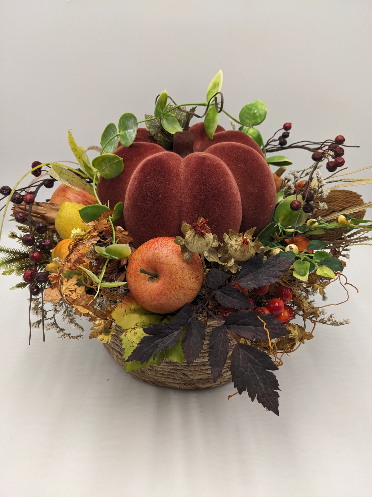 Herbstgesteck von vorn: Kürbis in Rotbraun, gelbe Birne, rote Beeren, Gräser und dunkles Laub im Korb