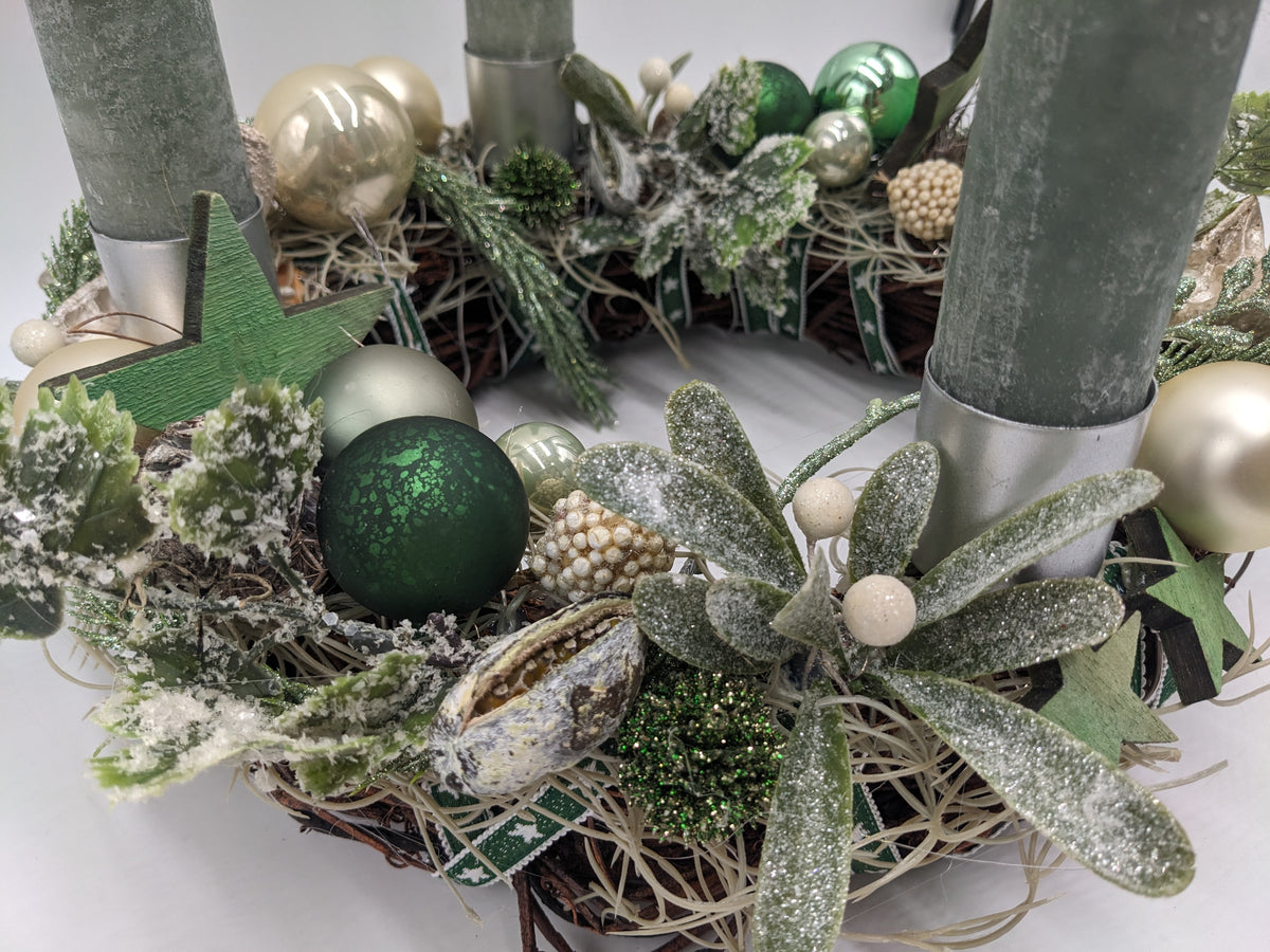 Nahaufnahme des Adventskranzes: dunkelgrüne Kugel, beschneite Mistelzweige mit weißen Beeren und grüner Holzstern
