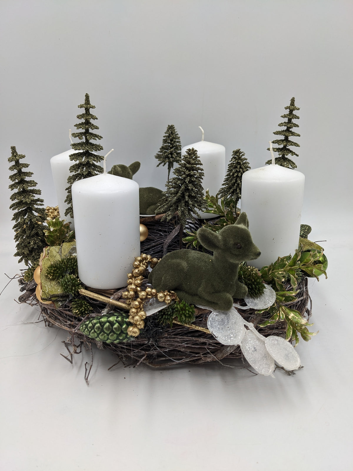 Adventskranz aus Zweigen mit vier weißen Kerzen, grünen Tannenbäumchen, Rehkitz und goldenen Beeren