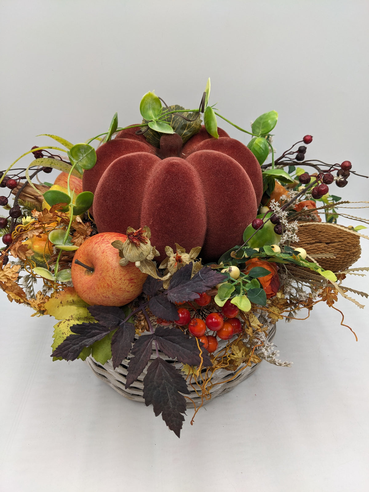 Herbstgesteck von schräg oben: Kürbis in der Mitte, ringsum Apfel, Beerenzweige, Gräser und Herbstlaub