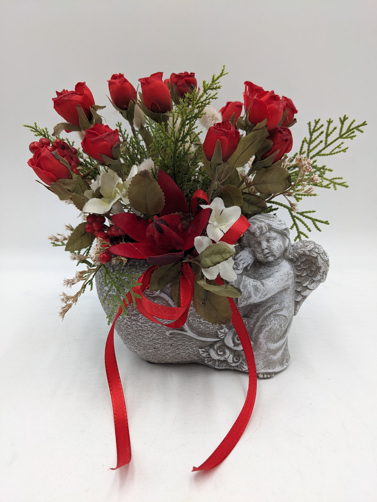 Graues Engelgefäß mit roten Rosen, weißen Blüten, Gräsern und roter Satinschleife von vorn