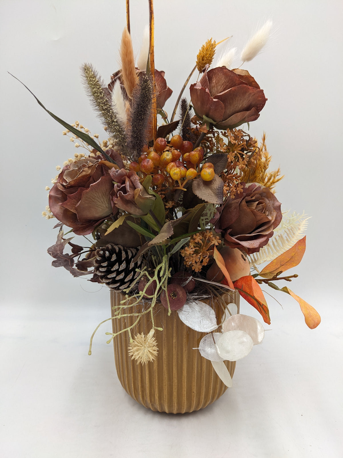 Herbstgesteck mit braunen Rosen, Zapfen, orangen Beeren und Gräsern in geriffeltem ockerfarbenem Keramiktopf