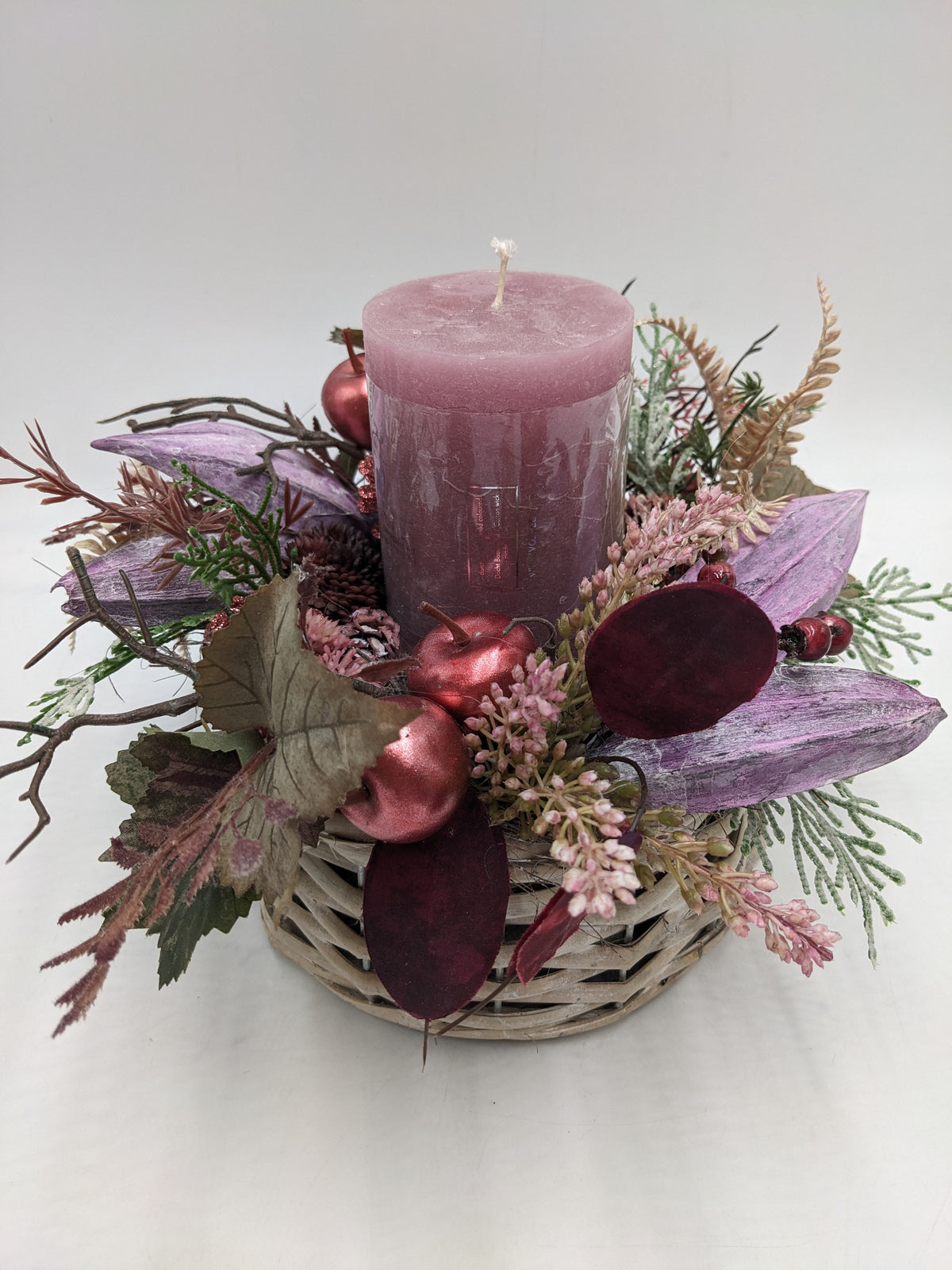 Tischgesteck in Rosa und Lila mit Stumpenkerze, Sedum, Heide, Zapfen und Beeren im grauen Korb von oben