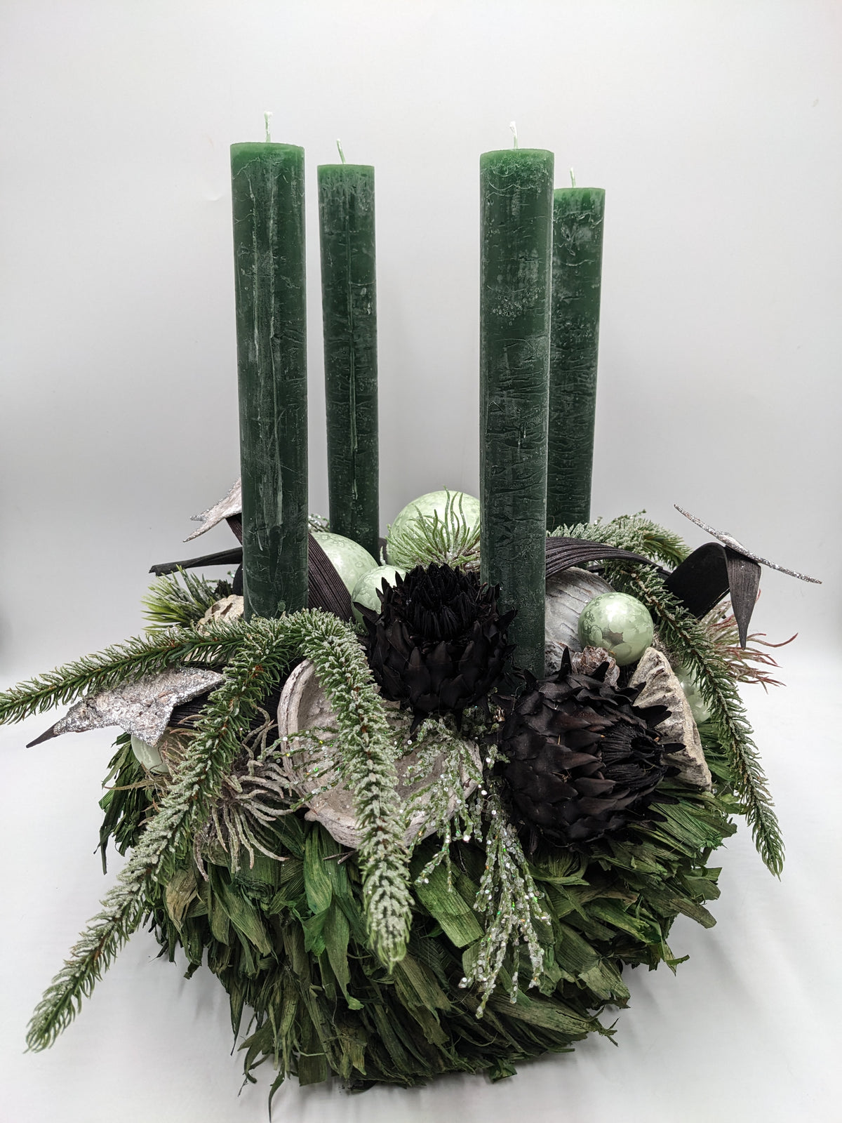 Adventskranz in Grün mit vier dunkelgrünen Stabkerzen, hellgrünen Kugeln, schwarzen Artischocken und Silbersternen