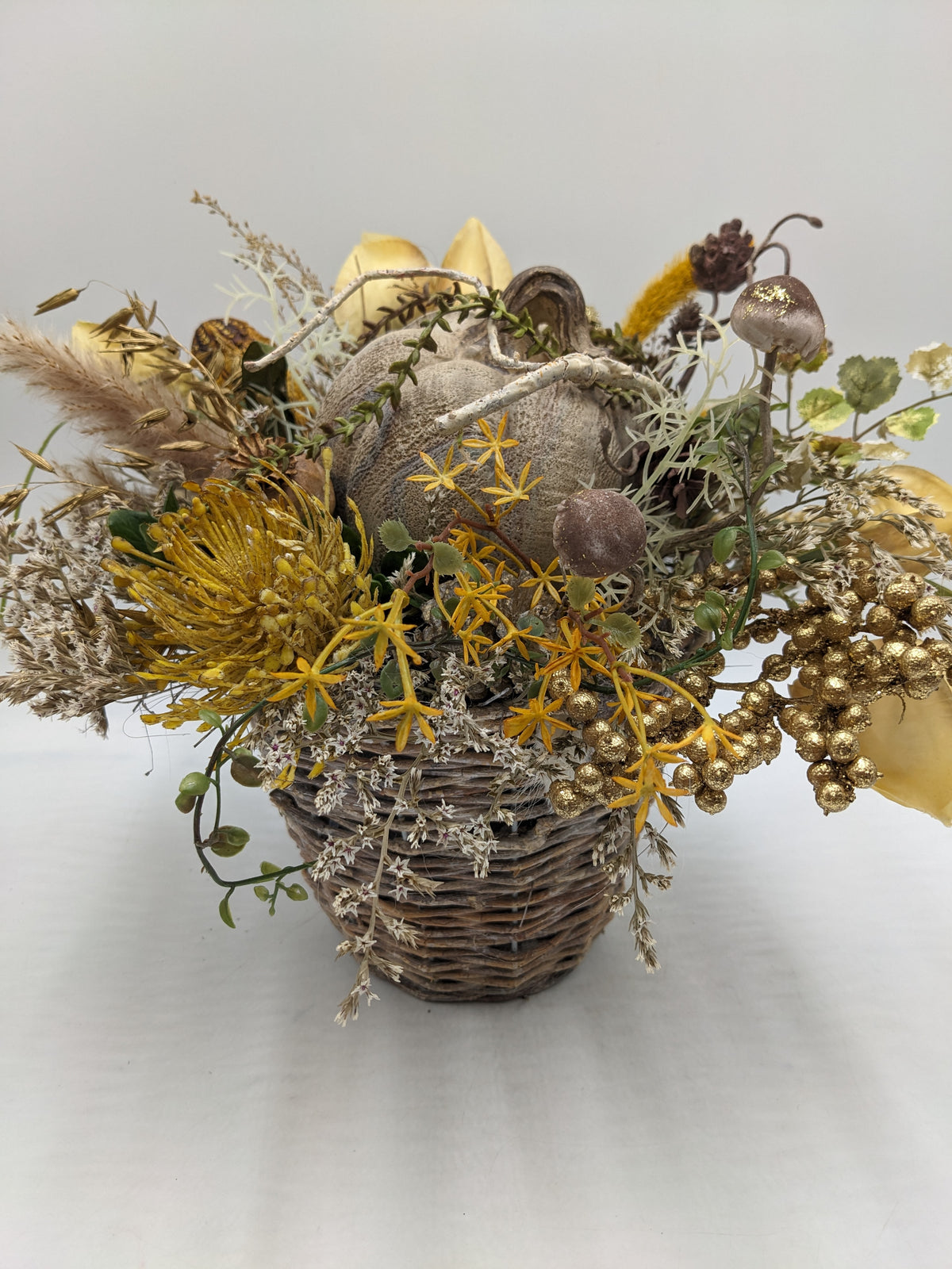 Herbstgesteck im Korb mit grauem Kürbis, gelber Spider-Blüte, Pilzen, Gräsern und goldenen Beeren