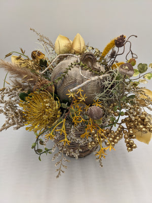 Herbstgesteck von oben: Kürbis mit hellem Ast, gelbe Sternblüten, Hafer, Rispen und cremefarbene Blätter