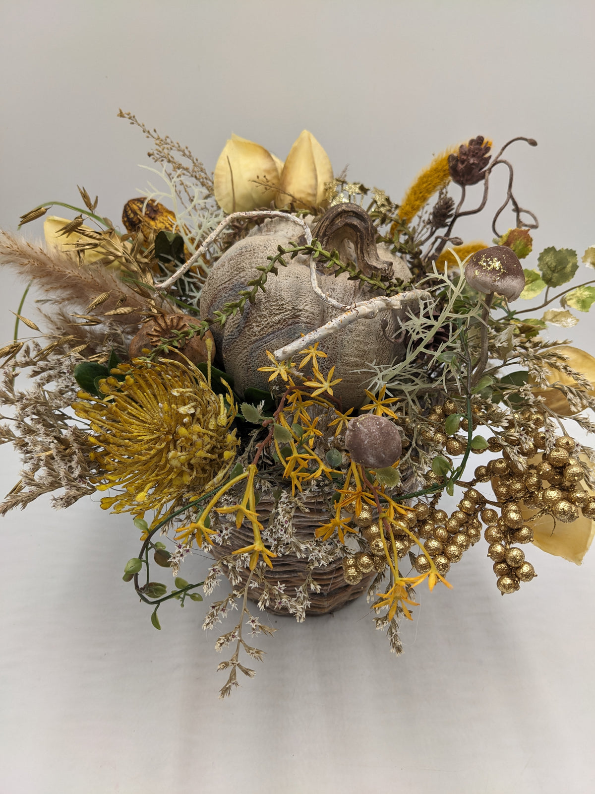 Herbstgesteck von oben: Kürbis mit hellem Ast, gelbe Sternblüten, Hafer, Rispen und cremefarbene Blätter