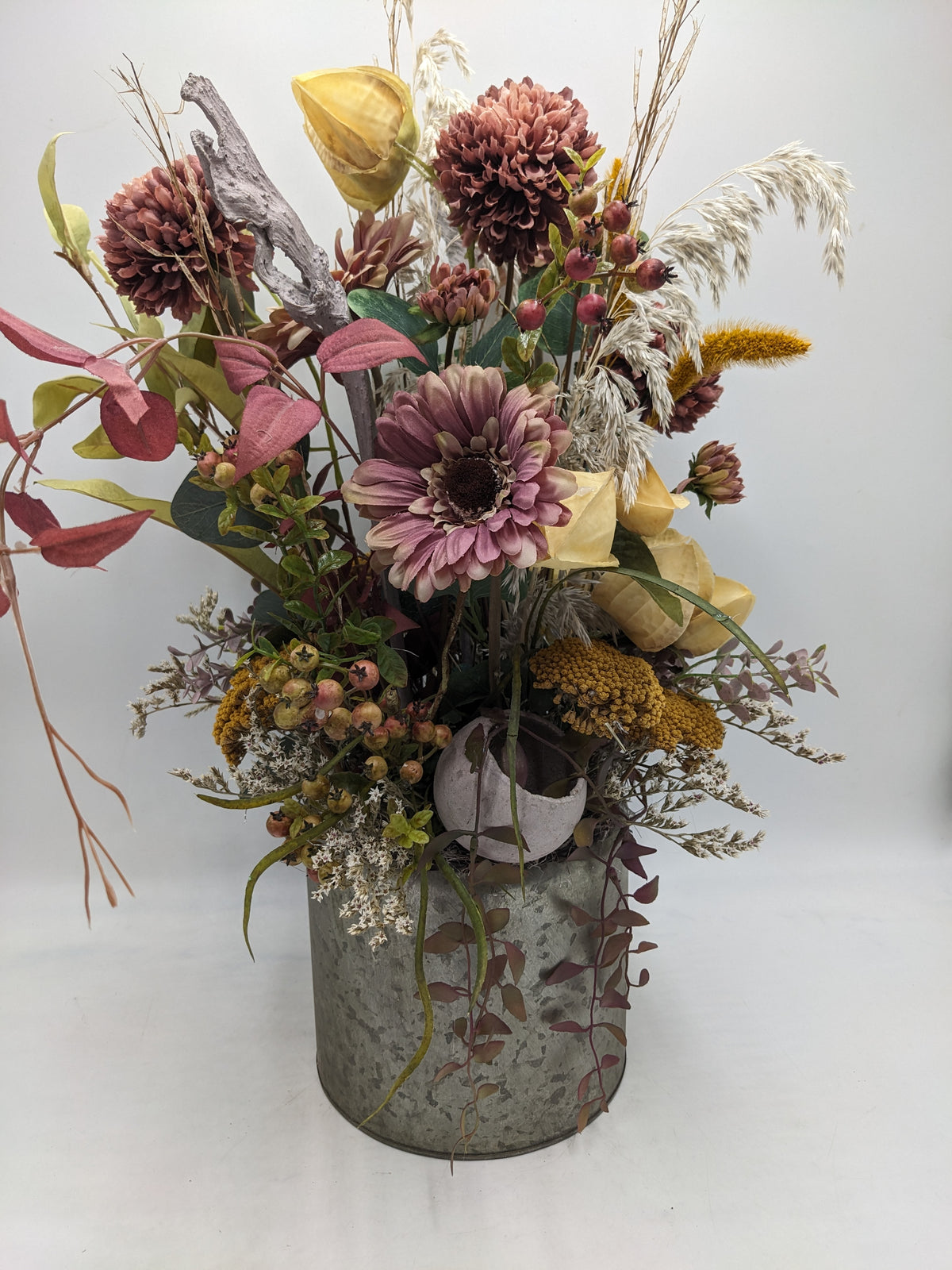 Hohes Herbstgesteck im Zinktopf mit altrosa Gerbera, Chrysanthemen, gelben Physalis und hellen Gräsern