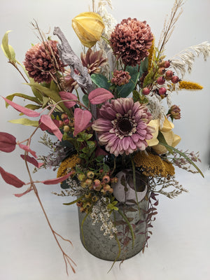 Herbstgesteck von schräg vorn: altrosa Gerbera, rote Beeren, gelbe Schafgarbe und rosa Blätter über grauem Zinktopf