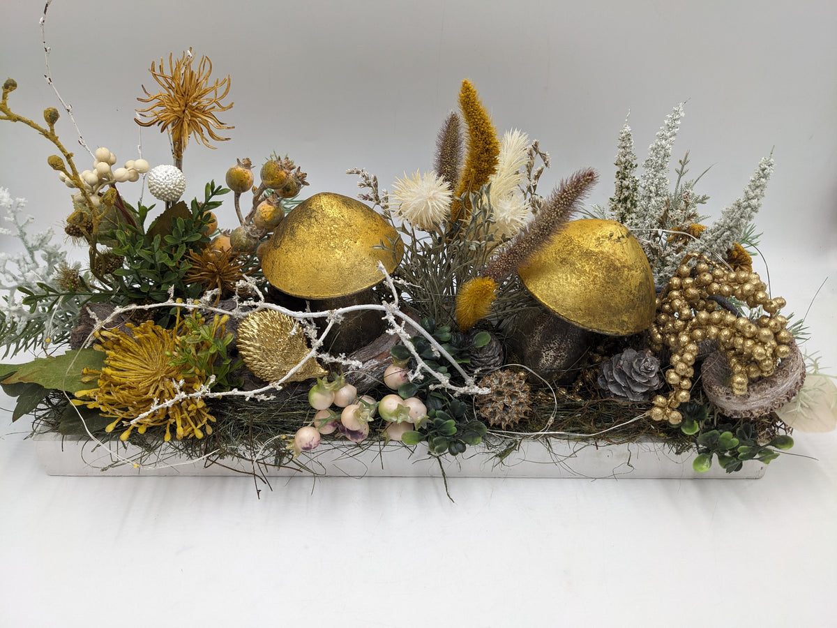 Herbstgesteck von vorn: goldene Pilze, gelbe Blüten, weiße Beeren, Zapfen und goldene Beerenranke im Tablett