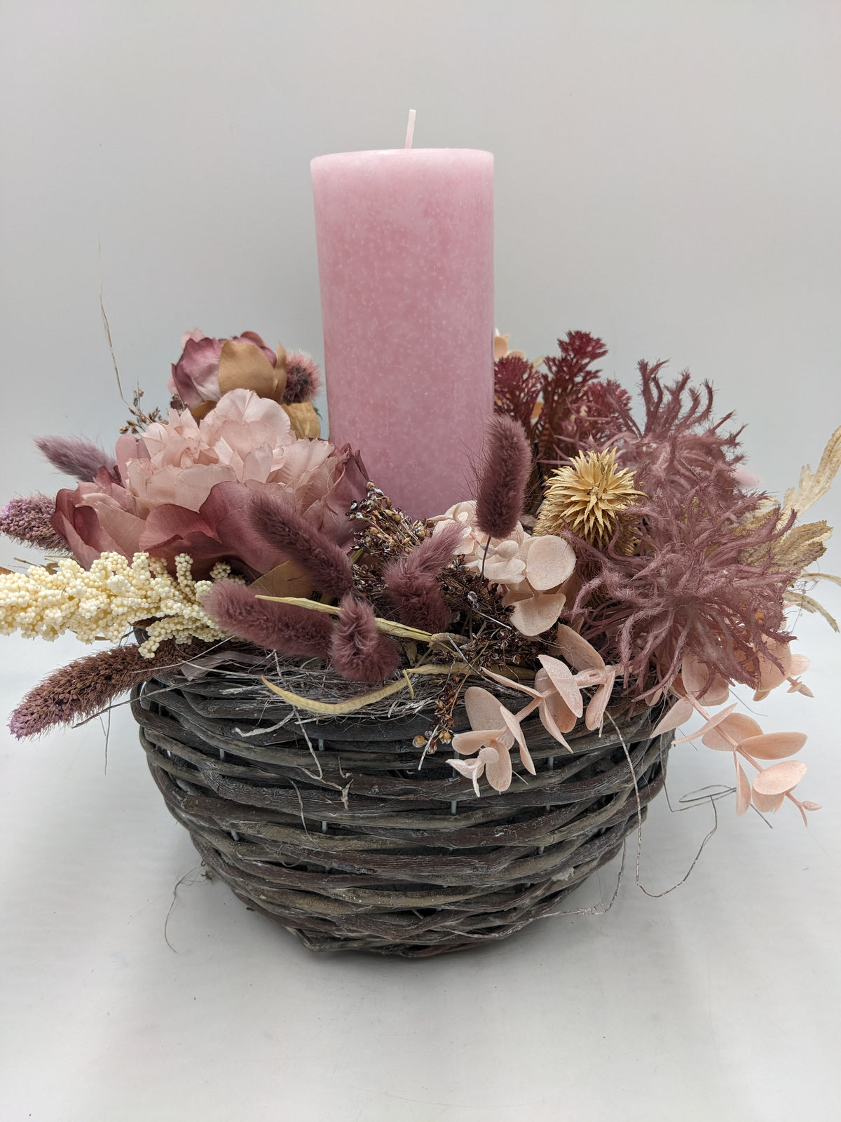Herbstgesteck im grauen Weidenkorb mit rosa Stumpenkerze, altrosa Rose, Spider und cremefarbenen Rispen