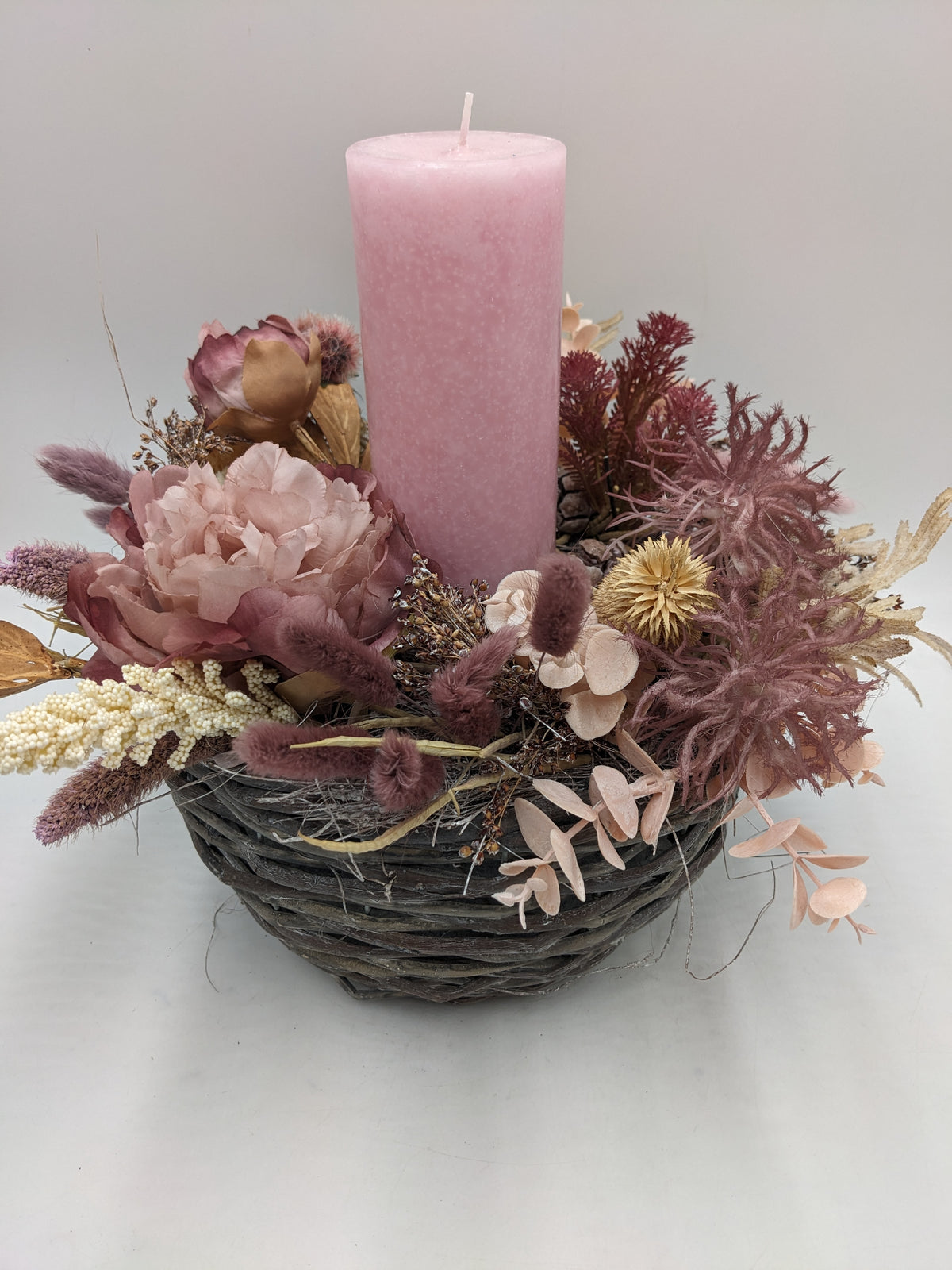 Tischgesteck von vorn: rosa Kerze im Korb, umgeben von Rosé-Rose, Lagurus-Gräsern und apricotfarbenem Eukalyptus