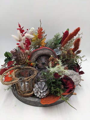 Herbstgesteck auf grauem Holztablett mit Keramik-Igel, Weidenwindlicht, Zapfen, Gräsern und roten Rispen