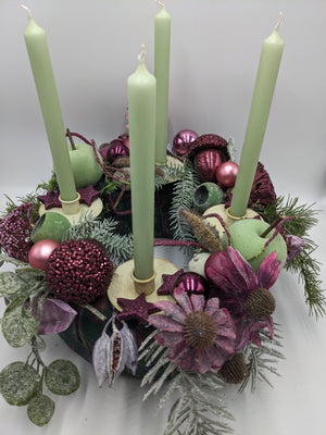 Adventskranz von oben: vier grüne Kerzen in cremefarbenen Haltern, Glitzersterne, Eichel und beschneite Zweige