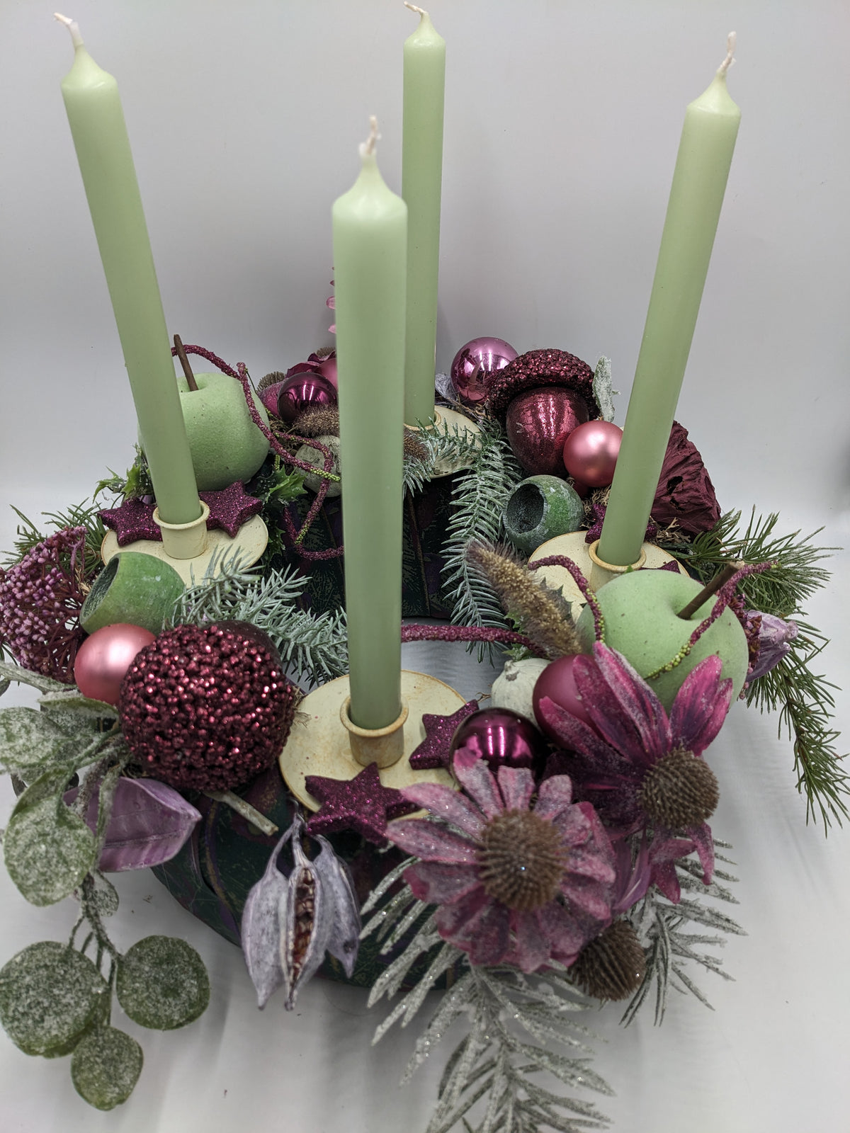 Adventskranz von oben: vier grüne Kerzen in cremefarbenen Haltern, Glitzersterne, Eichel und beschneite Zweige
