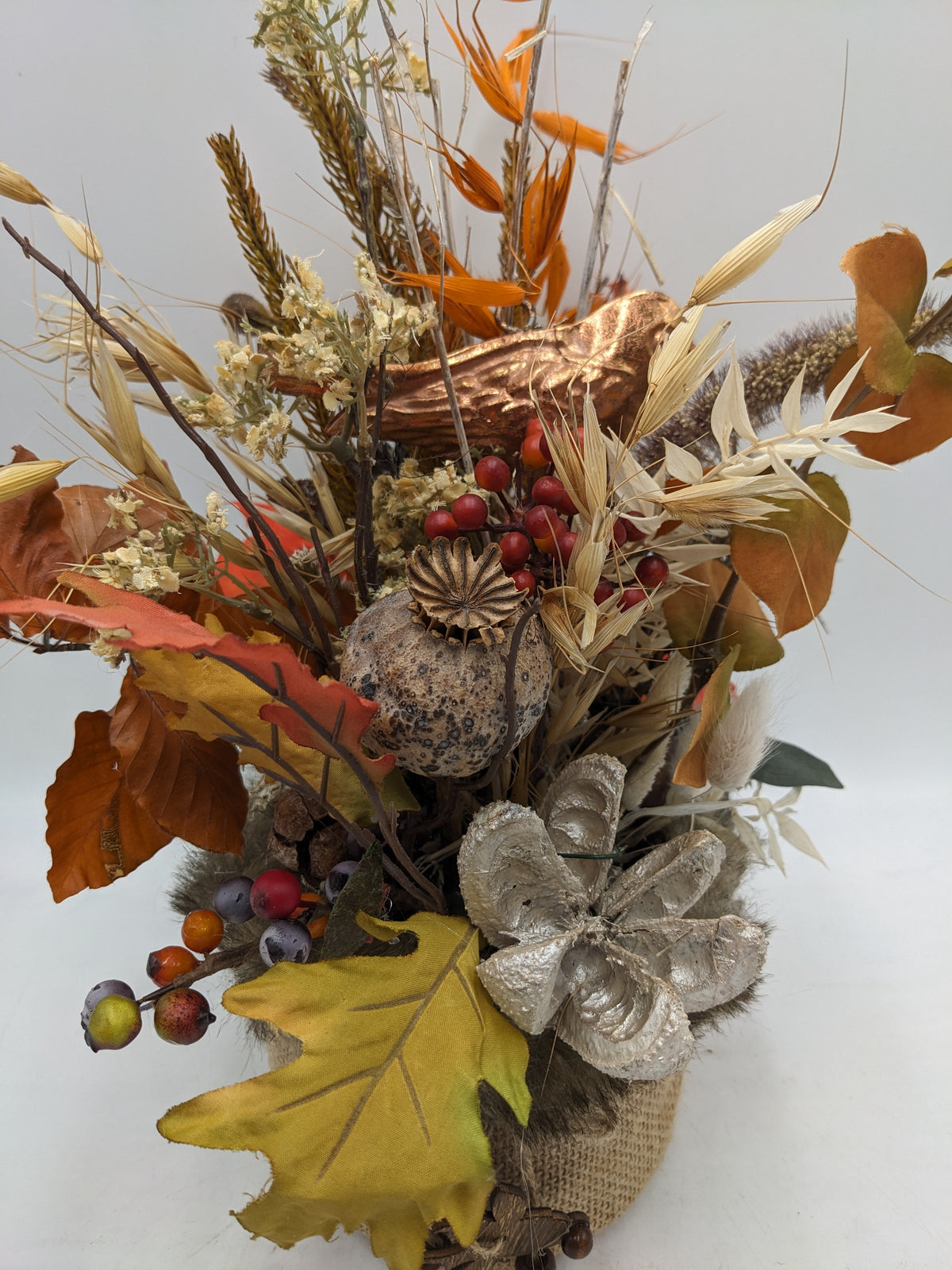Nahaufnahme des Herbstgestecks: Mohnkapsel, rote Beeren, gelbes Eichenblatt und silbrige Blüte