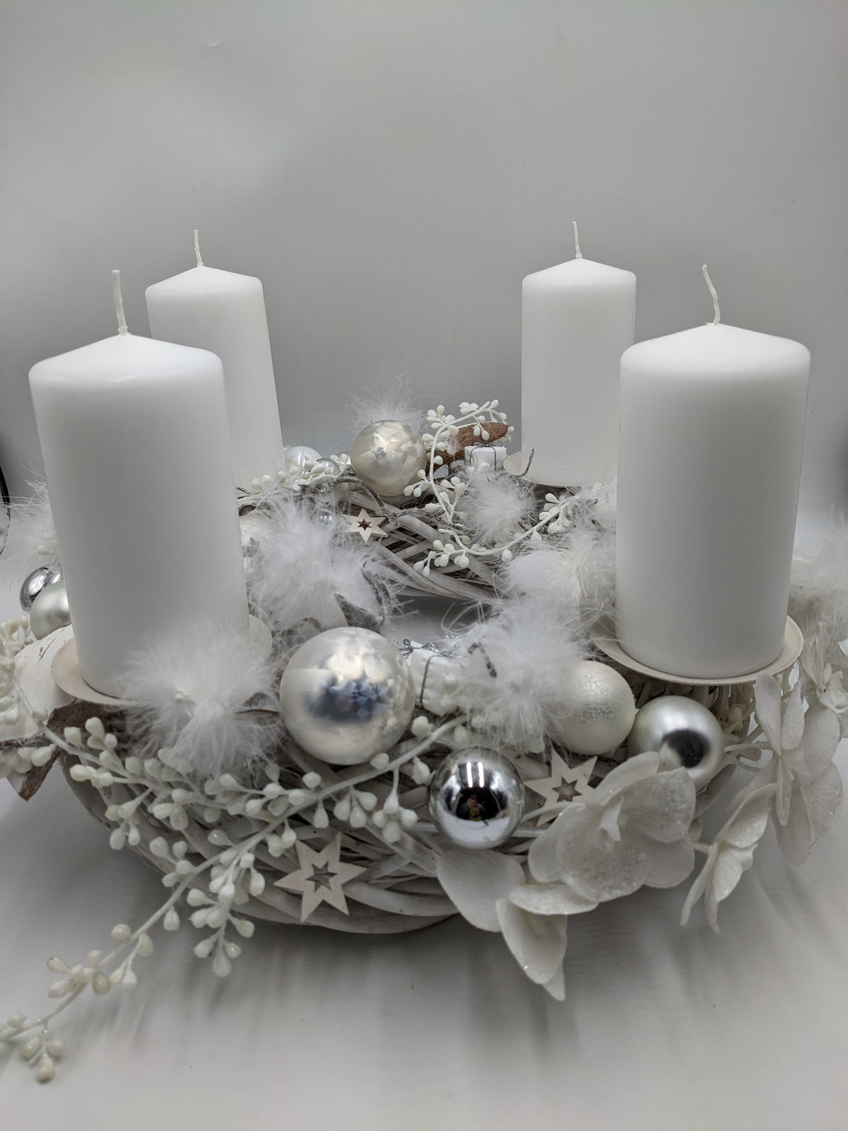 Adventskranz in Weiß und Silber mit vier weißen Stumpenkerzen, Kugeln, Federn und Holzsternen, seitlich fotografiert