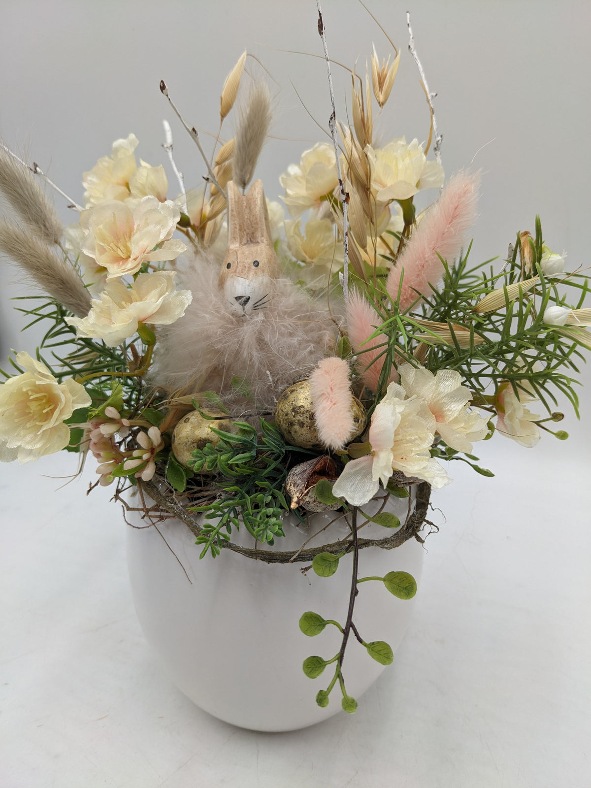 Ostergesteck von oben mit Hasenfigur, cremefarbenen Kirschblüten, rosa Gräsern und gesprenkelten Eiern
