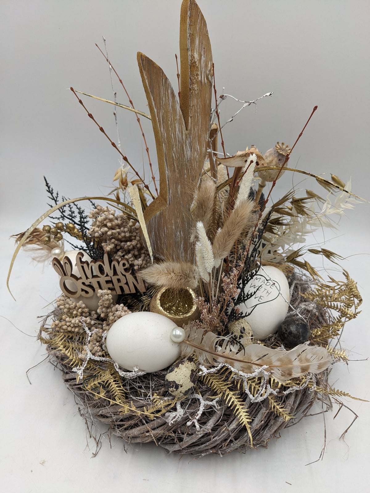 Ostergesteck im Rebenkranz mit hohem Holzhasen, weißen Eiern, Gräsern, Federn und goldenen Farnblättern