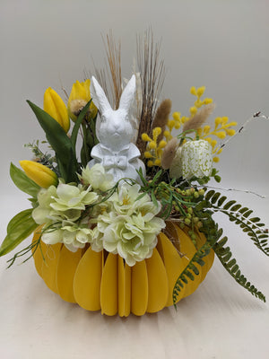 Ostergesteck in gelber Faltschale mit gelben Tulpen, cremefarbenen Blüten, Gräsern und weißer Hasenfigur