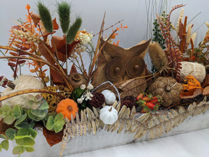 Herbstgesteck in Nahaufnahme: Eulenfigur, weiße Kürbisse, Zapfen, Beeren, grüne Blätter und Trockengräser