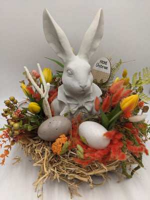 Osterarrangement von vorn: Hase mit Schleife, Schild Frohe Ostern, Tulpen, Farn, Beeren und Eier im Nest