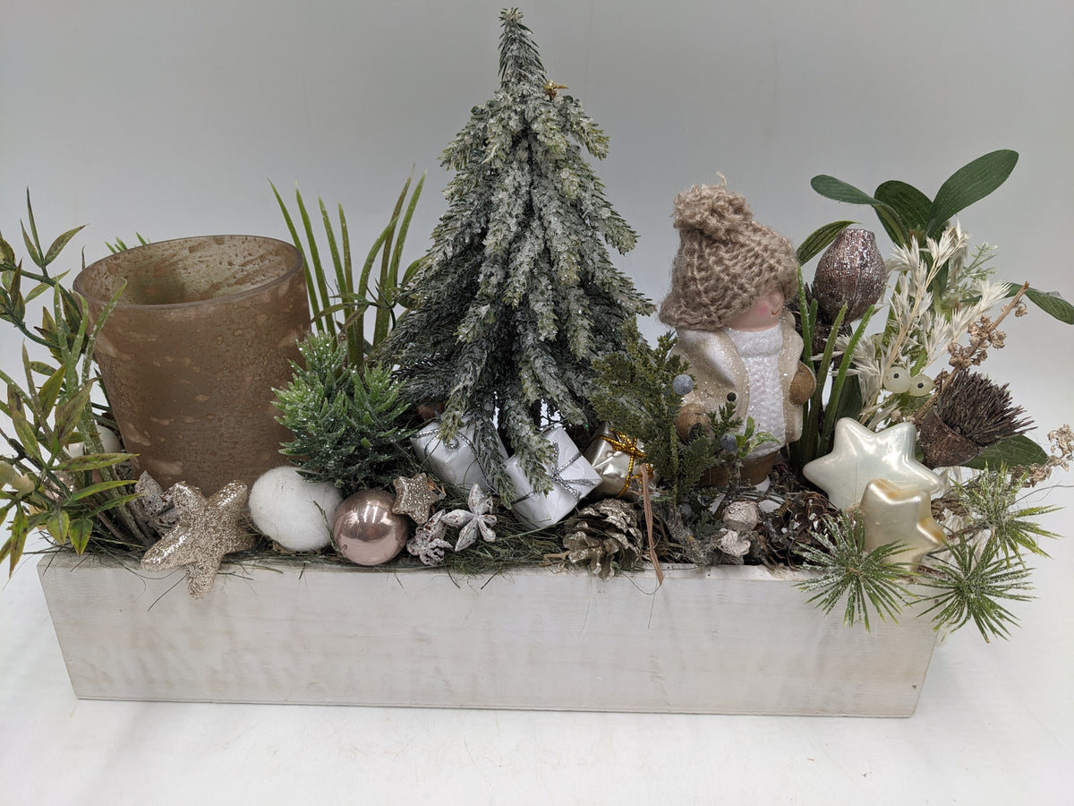 Wintergesteck in weißer Holzschale mit verschneitem Tannenbaum, Wichtelfigur, Zapfen und braunem Teelichtglas