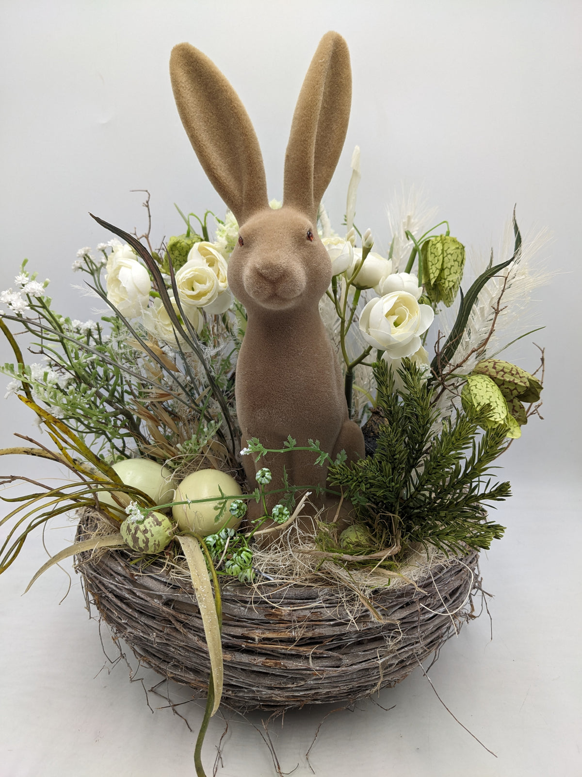 Ostergesteck im Rebennest mit braunem Samthasen, weißen Ranunkeln, Schachbrettblumen und hellgrünen Eiern