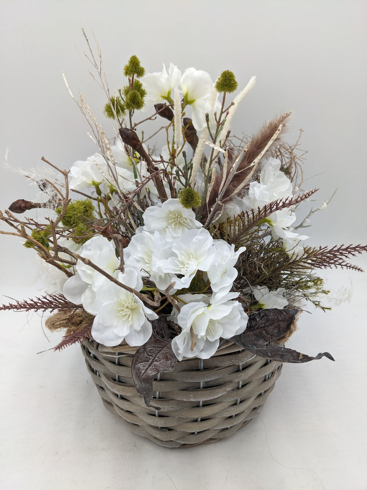 Frühlingsgesteck mit weißen Kirschblüten, Zweigen, Gräsern und grünen Kugelblüten im grauen Flechtkorb, von oben