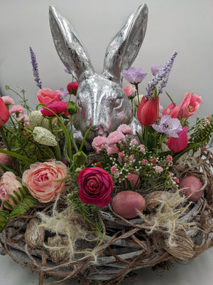 Ostergesteck im Nest mit silbernem Hasen, pinken Tulpen, Ranunkeln und altrosa Eiern in Nahaufnahme