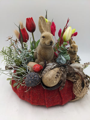 Frühlingsgesteck von vorn: Hasen, rote Tulpen, Eukalyptus, Federn, Zapfen und rot gesprenkeltes Ei