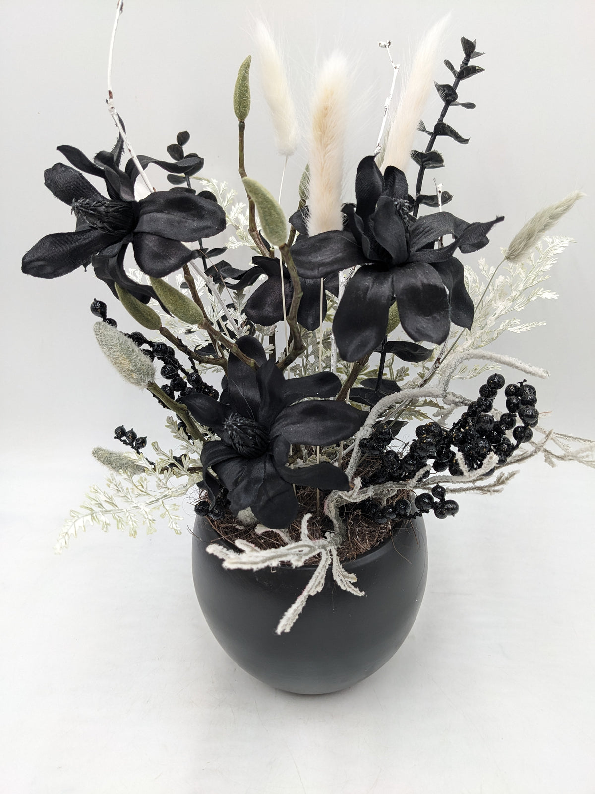 Nahansicht des schwarz-weißen Gestecks mit drei Magnolienblüten, bereiften Zweigen und Beerenrispen