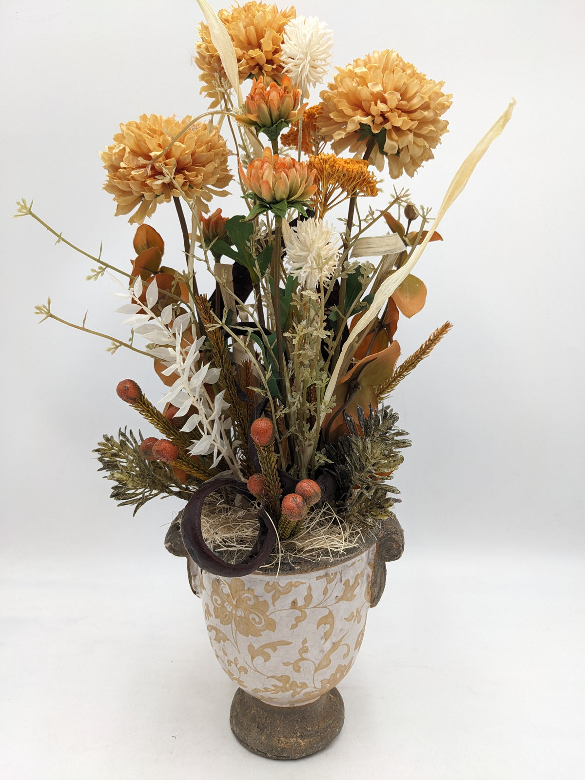 Hohes Gesteck mit apricotfarbenen Chrysanthemen, weißen Disteln und Gräsern in cremefarbenem Vintage-Pokal