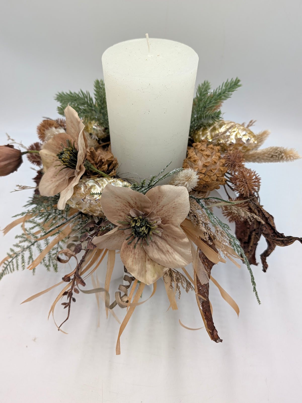 Winterkranz von oben mit beigen Christrosen, goldenen Zapfen, Tannengrün und weißer Stumpenkerze