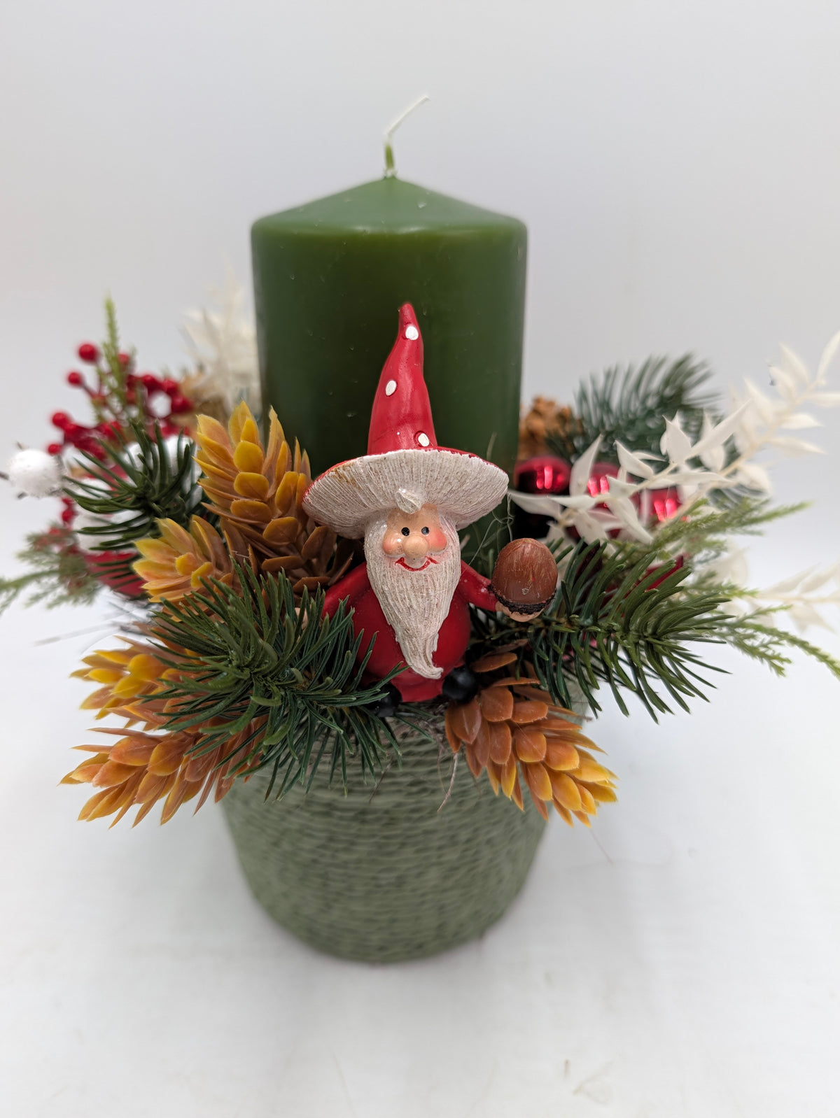 Weihnachtsgesteck mit grüner Stumpenkerze, Wichtelfigur, roten Beeren und Tannengrün im grünen Gefäß