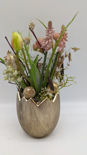 Ostergesteck im goldenen Eiertopf mit rosa Traubenhyazinthen, gelber Tulpe, Holzhase, Wachtelei und Schneckenhaus