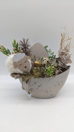 Ostergesteck in grauer Eierschale mit Holzschäfchen, goldenem und gesprenkeltem Ei, Gräsern und Eukalyptus