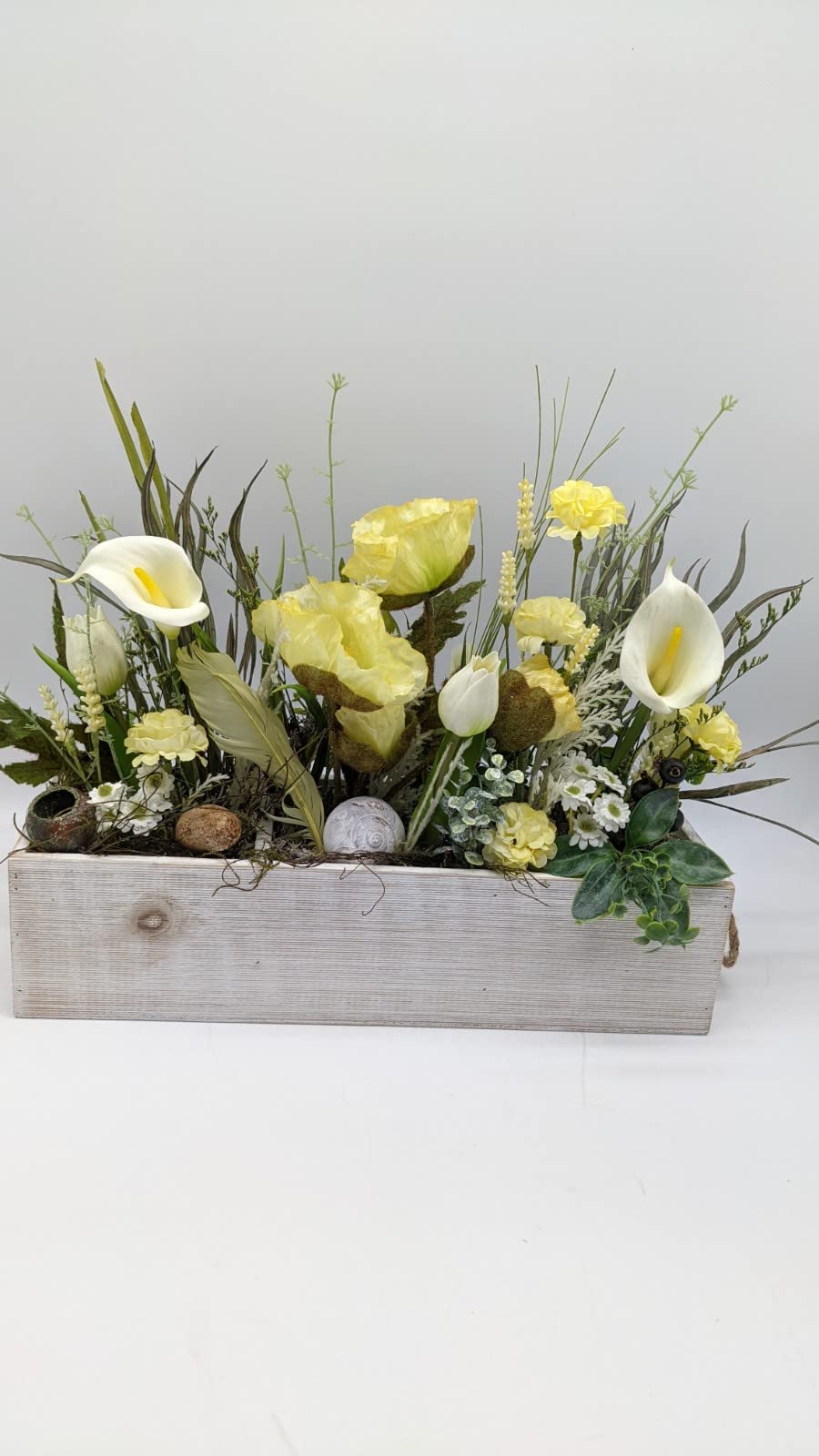 Ostergesteck von vorn: gelbe Mohnblüten, weiße Calla, Tulpen und Margeriten in weiß gekalktem Holzkasten