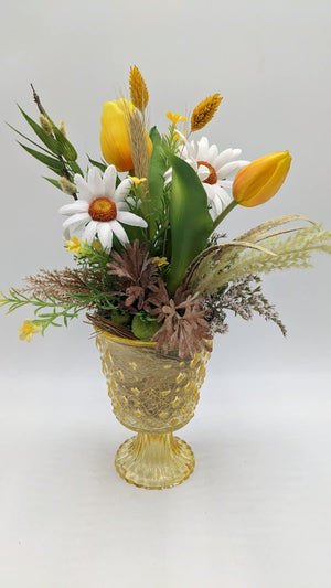 Frühlingsgesteck mit gelben Tulpen, weißen Margeriten, Ähren und Kätzchen in gelbem Glaspokal